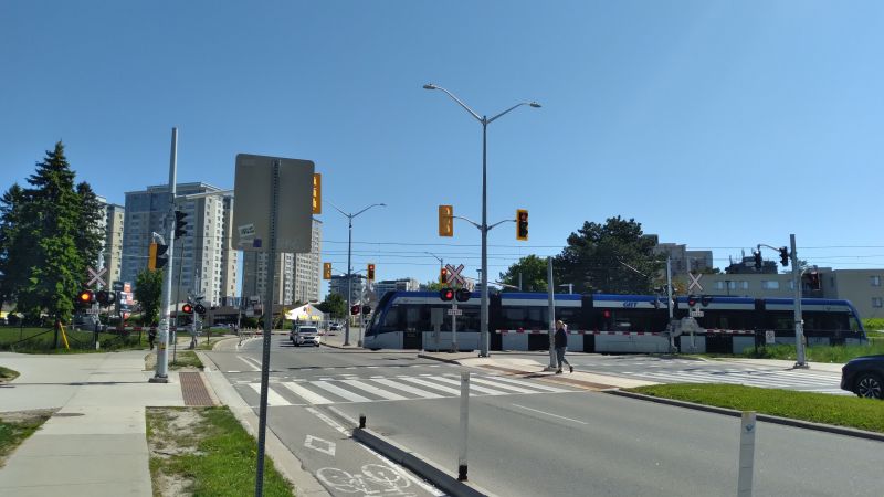 A rail crossing with traffic signals and a pedestrian/cyclist 
        crossing